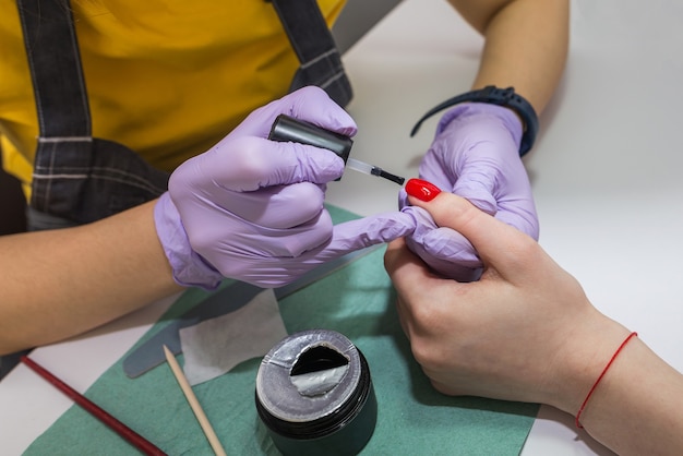 Girl master fait une manucure à un client dans un salon de manucure. Le maître couvre les ongles de vernis rouge. Concept de soins des ongles