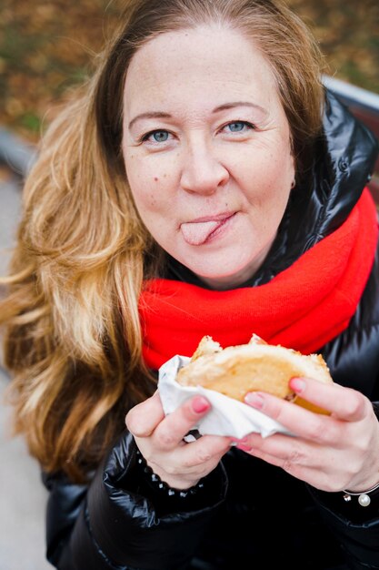 Girlwoman eating big hamburgercheeseburgerJunk gras savoureux street foodTake away burgerPause déjeuner à l'extérieur dans le parc assis sur un bancRégime malsainWeek-end relaxCorps positifProblèmes de surpoids