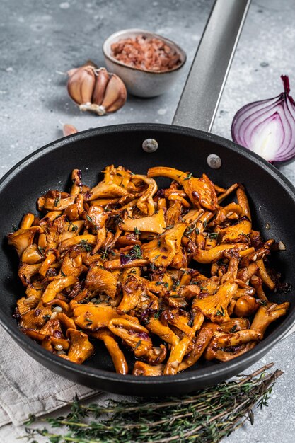 Girolles sautées aux oignons et au thym dans une poêle. Fond gris. Vue de dessus.