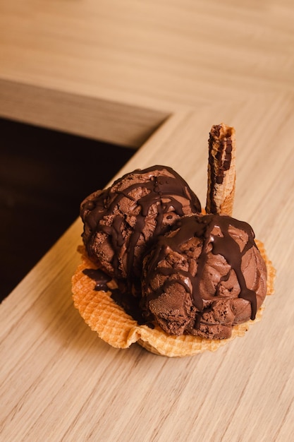 Glace au chocolat dans un bol à gaufres avec du chocolat fondu sur une table en bois