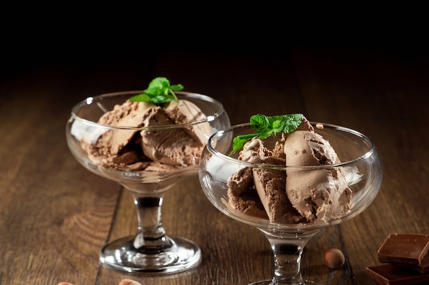 Glace au chocolat faite maison avec des feuilles de menthe, saupoudrée de chocolat dans un bol en verre sur une table en bois