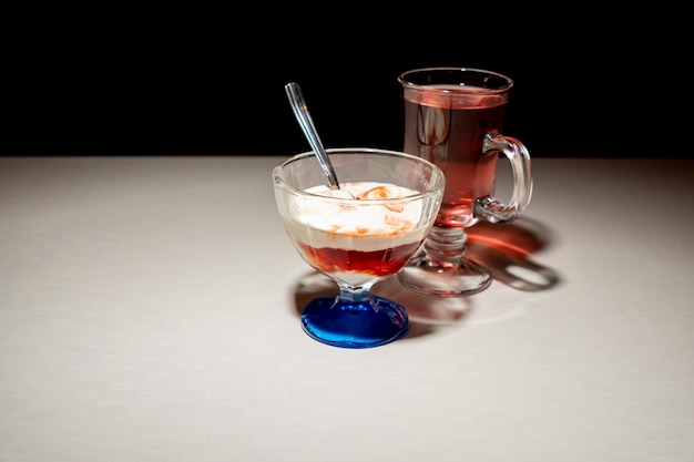 Glace au sirop dans un bol en verre sur une table lumineuse à côté d'un thé punch Fond sombre