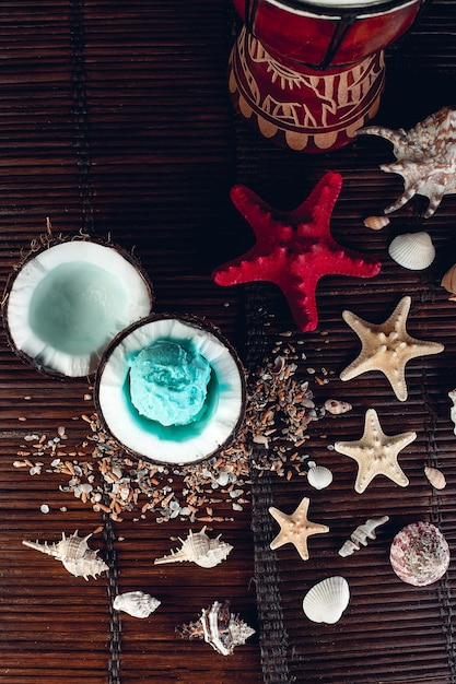 Glace bleue dans un bol de noix de coco près du sable, des coquillages, des étoiles de mer. Vue de dessus.