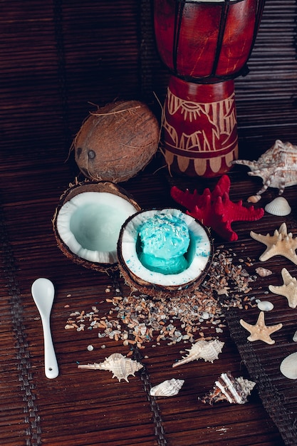 Glace bleue dans un bol de noix de coco près du sable, des coquillages, des étoiles de mer.