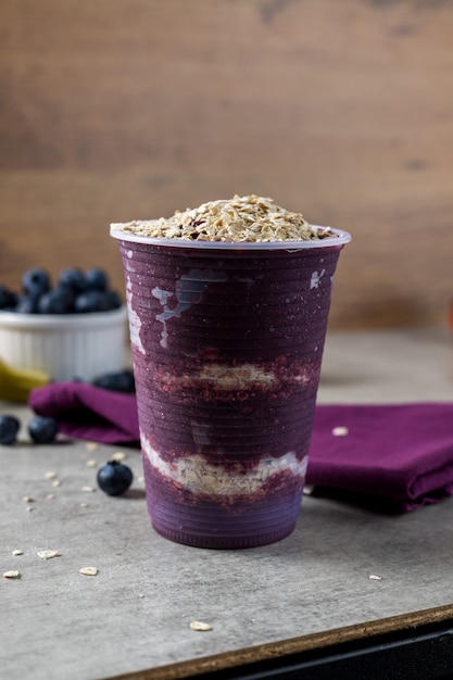 Glace congelée brésilienne et aux baies d'açai sur une tasse en plastique avec des flocons d'avoine. bananes, fraises et myrtilles sur fond. fond de bois. Vue de face du menu d'été.