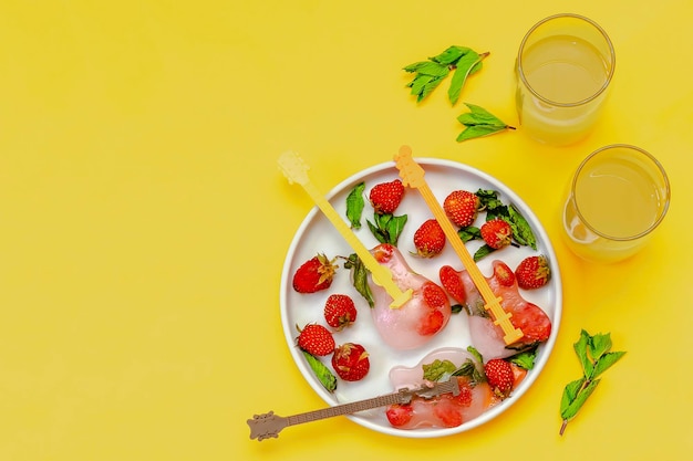 Glace congelée avec de la menthe aux fraises rouges en forme de guitare pour des cocktails de limonade d'été frais et froids avec du jus d'orange Crème glacée aux fruits sucrés faits maison sucettes glacées dessert sur plaque grise