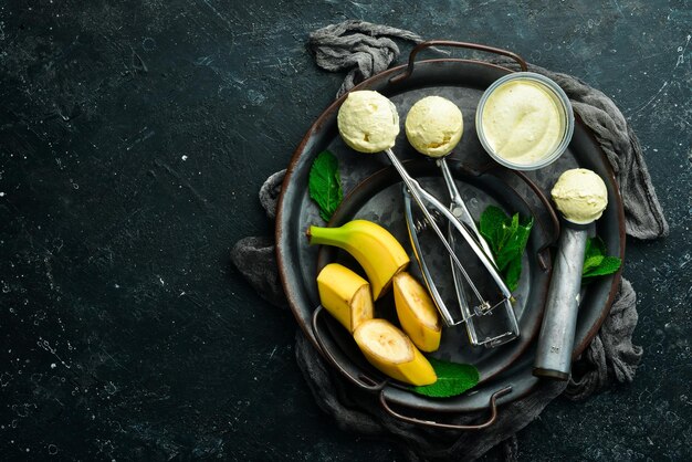 Glace jaune banane à la menthe et banane fraîche. Cuillère à glace. Sur un fond de pierre noire, vue de dessus.