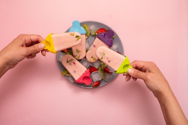 Glace maison à partir de moules dans des mains féminines sur une assiette avec de la glace et des morceaux de fruits sur fond coloré Vue de dessus