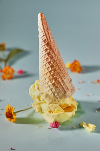 Glace à la mangue avec cornet gaufré sur fond bleu avec des fleurs jaunes.