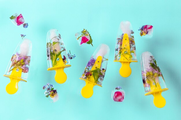 Glace popsicles volantes avec des fleurs et des glaçons sur une table pastel