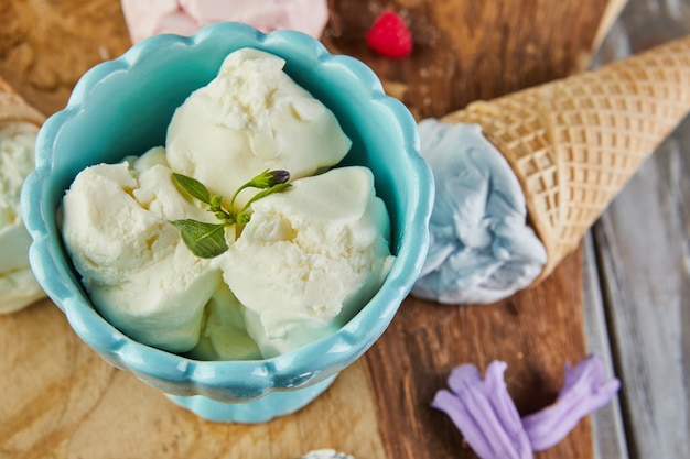 Glace vanille, myrtille et framboise en cornets gaufrés et glace en coupe sur planche de bois avec baies et fleurs.