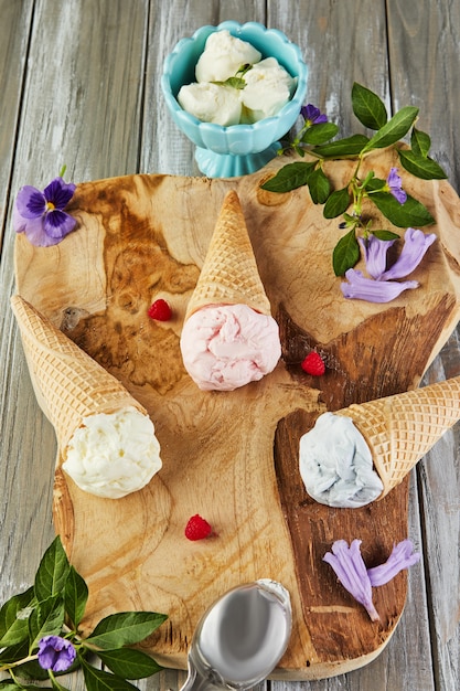 Glace vanille, myrtille et framboise dans des cornets gaufrés sur planche de bois avec des baies et des fleurs.