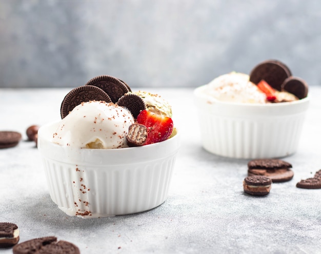 Glace à la vanille et pistache dans un bol en céramique blanche décorée de chocolat, de biscuits Oreo et de fraise