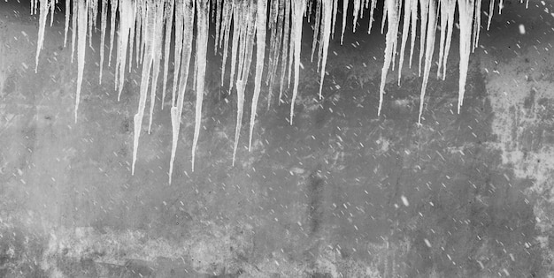 Les glaçons accrochés au toit contre le mur gris