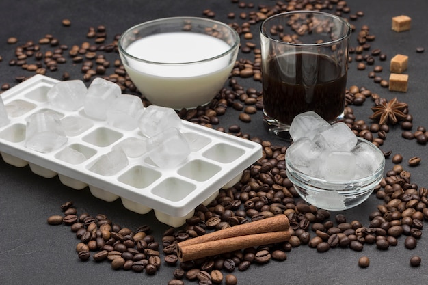 Glaçons dans un bol en verre, verre de lait et verre de café. Grains de café et bâtons de cannelle