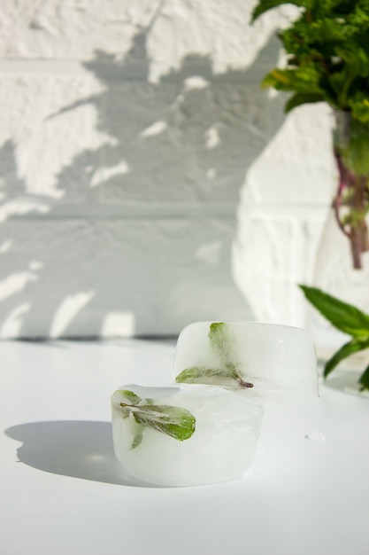 Glaçons avec des feuilles de menthe verte à l'intérieur, sur un mur blanc, place pour le texte.