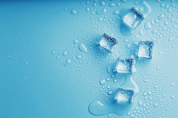 Glaçons avec des gouttes d'eau de fonte sur une table bleue, vue du dessus. Fraîcheur sous la chaleur sensuelle. Boissons rafraîchissantes