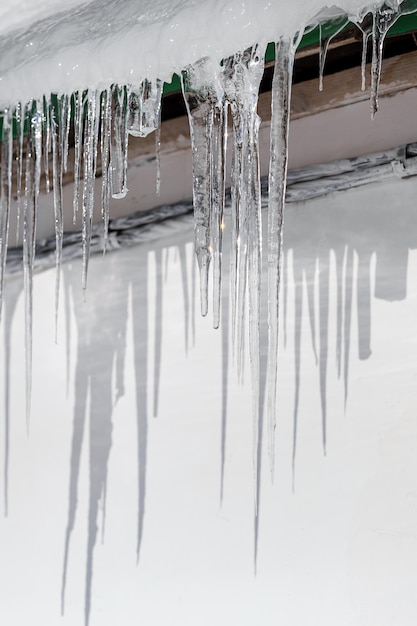 Des glaçons pendent du toit sur un mur blanc et brillent à sunxA