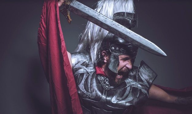 Gladiateur romain, lutteur et guerrier de Rome avec casque et manteau rouge, porte une épée de fer, une barbe et des cheveux longs.