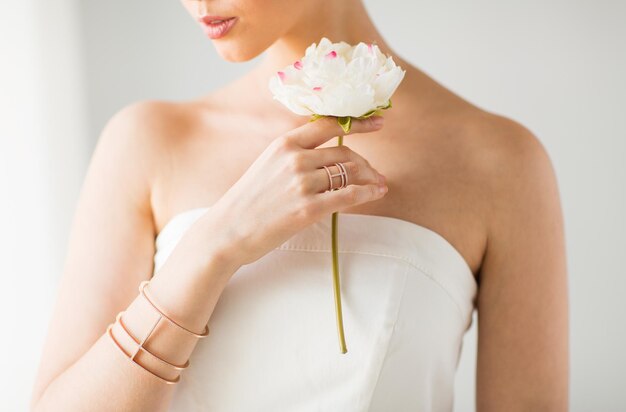 glamour, beauté, bijoux et concept de luxe - gros plan d'une belle femme avec une bague en or et un bracelet tenant une fleur