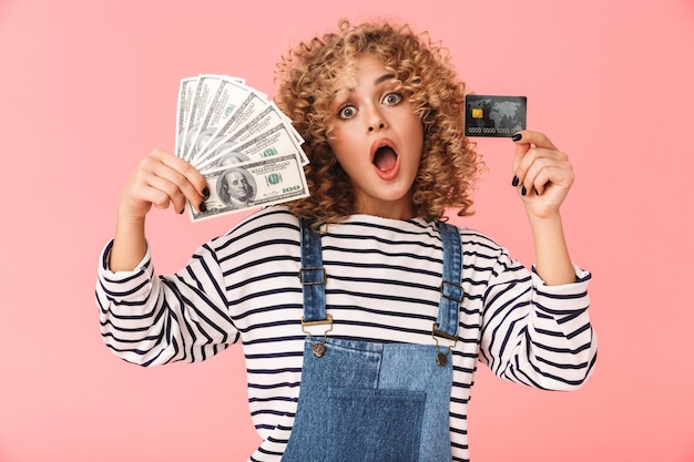 Glamour curly woman 20s holding fan d'argent dollar et carte de crédit en position debout