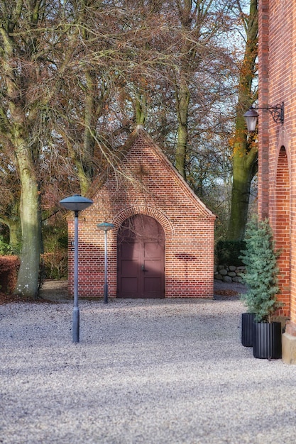 Église nationale danoise entourée d'arbres et de plantes de forêts de feuillus non cultivés et dans l'arrière-cour Bâtiment en brique rouge à l'architecture traditionnelle avec cour en pierre et lumières à l'extérieur