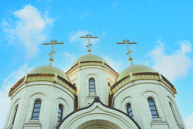 Église orthodoxe en briques avec dômes dorés et 3 croix sur fond de beau ciel nuageux.