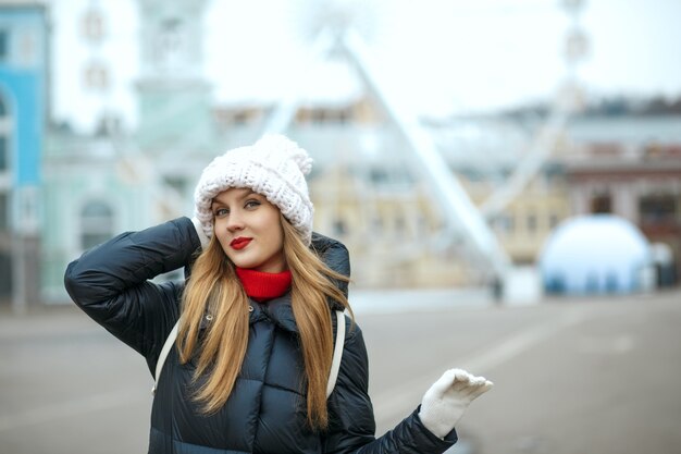 Glorieuse femme blonde au rouge à lèvres portant un bonnet tricoté, profitant d'une promenade en ville. Espace pour le texte