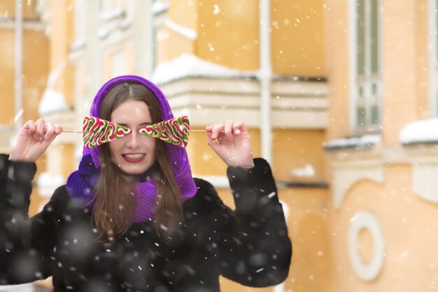 Glorieuse femme brune s'amusant avec des sucettes colorées dans la rue avec des flocons de neige. Espace pour le texte