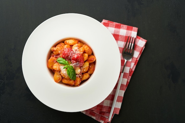 Gnocchi de pomme de terre Gnocchi traditionnel de pommes de terre fait maison avec sauce tomate basilic et fromage parmesan sur la table de cuisine sur fond de table de cuisine noire Nourriture italienne traditionnelle Vue supérieure