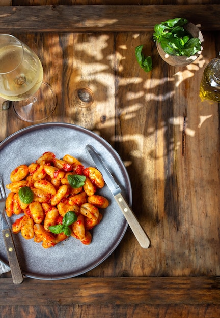 Gnocchi de pommes de terre italien traditionnel avec sauce tomate et basilic frais avec verre de vin blanc fond rustique