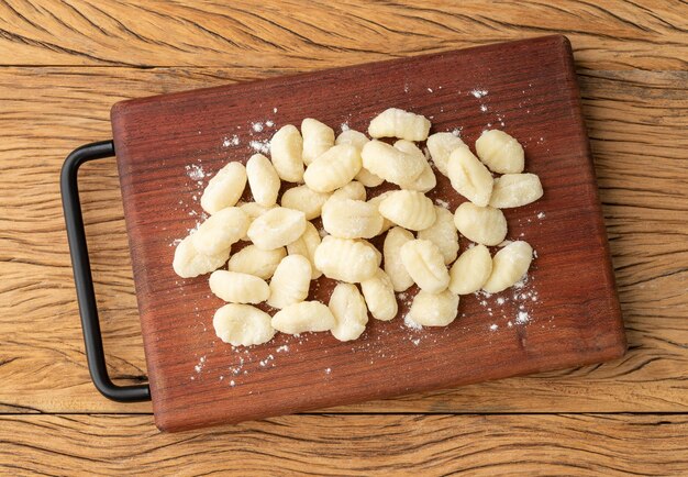 Gnocchis de pâtes italiennes non cuites sur une planche au-dessus d'une table en bois.