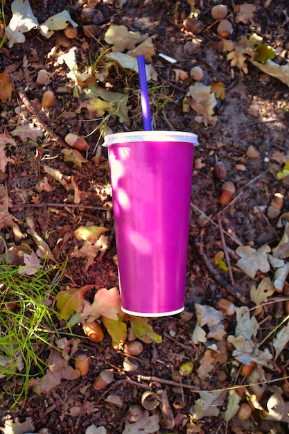 Gobelet en papier avec couvercle en plastique et paille jetée dans la forêt sur le papier soda au sol