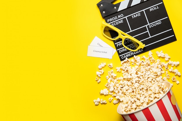 Gobelet en papier avec pop-corn et battant de film sur fond jaune, place pour le texte