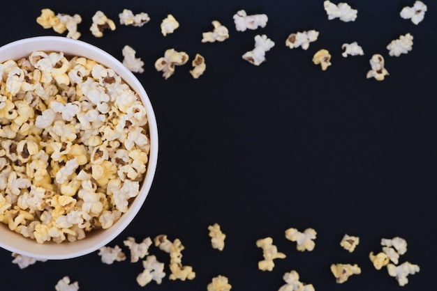 Gobelet en papier avec pop-corn et pop-corn éparpillés sur un fond noir, vue de dessus, copyspace.