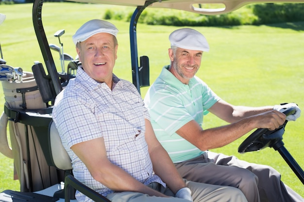 Golfer des amis conduisant dans leur buggy de golf souriant à la caméra