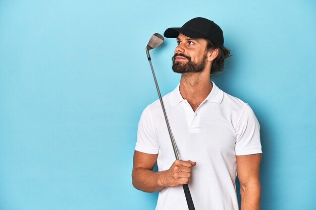 Photo un golfeur aux cheveux longs barbu tenant un club de golf dans un studio bleu