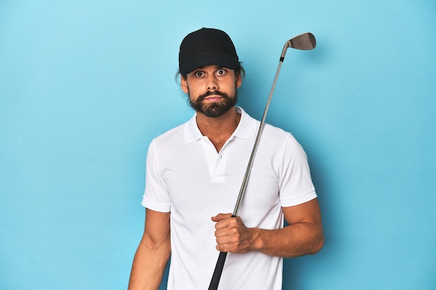 Photo golfeur aux cheveux longs avec club et chapeau hausse les épaules et les yeux ouverts confus