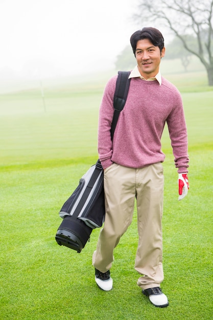 Golfeur debout tenant son sac de golf souriant à la caméra