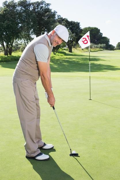 Golfeur sur le putting green au dix-huitième trou souriant à la caméra