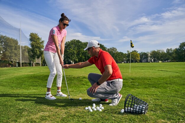 Golfeuse débutante aux cheveux noirs focalisée pratiquant une bonne technique de préhension assistée par son instructeur masculin