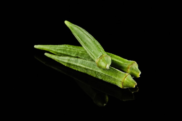 Gombo frais ou roselle verte sur une surface noire avec reflet.