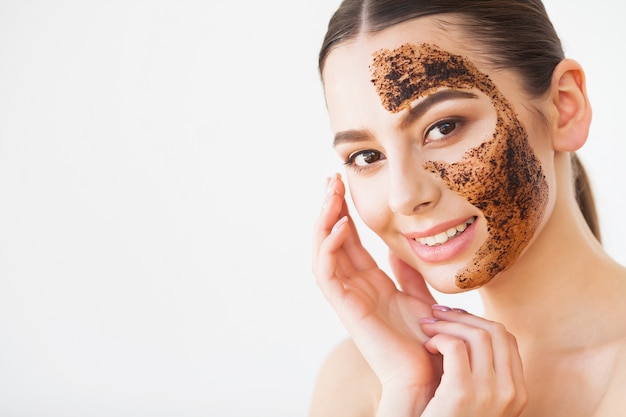 Gommage de la peau du visage. Jeune fille souriante appliquant un gommage au masque au café sur la peau.