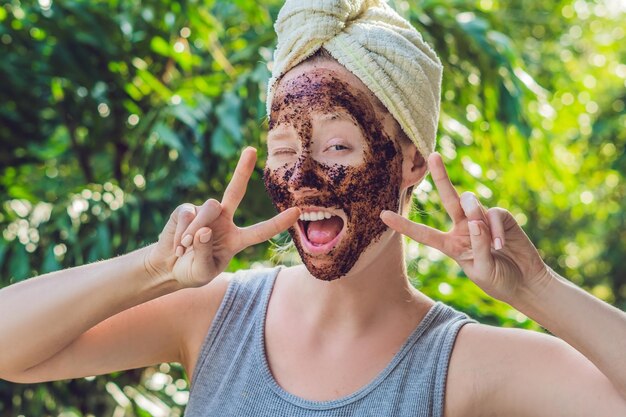 Gommage de la peau du visage. Portrait de modèle féminin souriant sexy appliquant un masque de café naturel, gommage du visage sur la peau du visage. Gros plan de la belle femme heureuse avec le visage couvert de produit de beauté. Haute résolution.