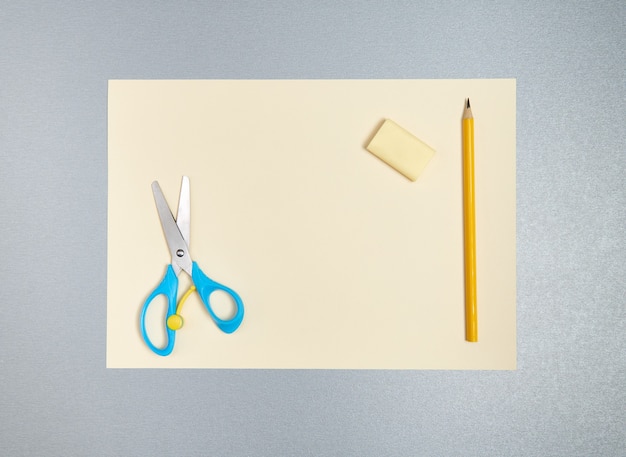 Gomme, crayon et ciseaux sur une feuille de papier jaune. Vue de dessus, à plat sur un fond gris