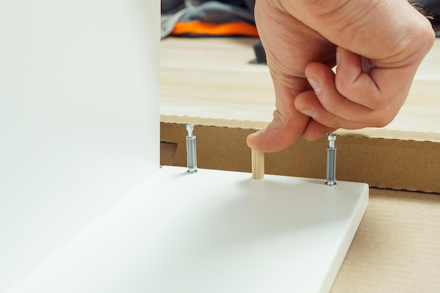 Goujon en bois de doigt de mains masculines pour fixer des murs de tiroir blanc assemblant une commode ou une armoire Liens de meubles excentriques