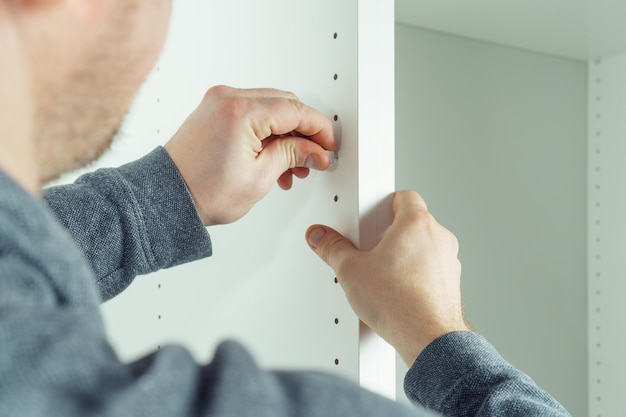 Goujon en bois de doigt de mains masculines pour fixer des murs de tiroir blanc assemblant une commode ou une armoire Liens de meubles excentriques