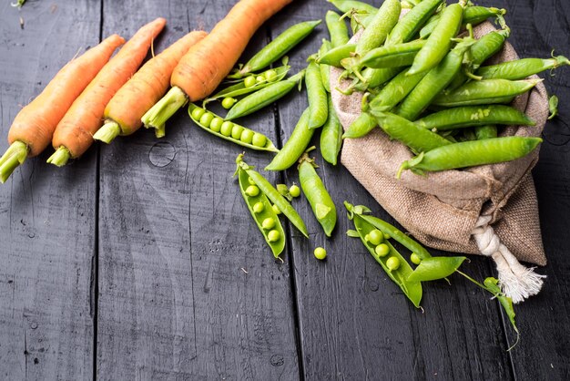 Gousses de pois et de carottes dans un sac sur fond de bois noir