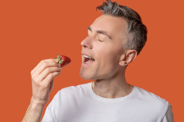 Goût incroyable. Homme heureux avec les yeux fermés apportant des fraises savoureuses juteuses à la bouche ouverte