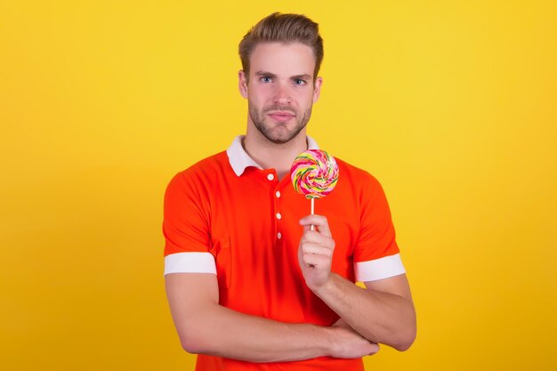 Goûte l'arc-en-ciel. Fond jaune bonbon homme. Un beau mec tient des bonbons sur un bâton. Boutique de bonbons. Sucette ou ventouse. Gâterie sucrée. Fabrique de bonbons et confiserie.